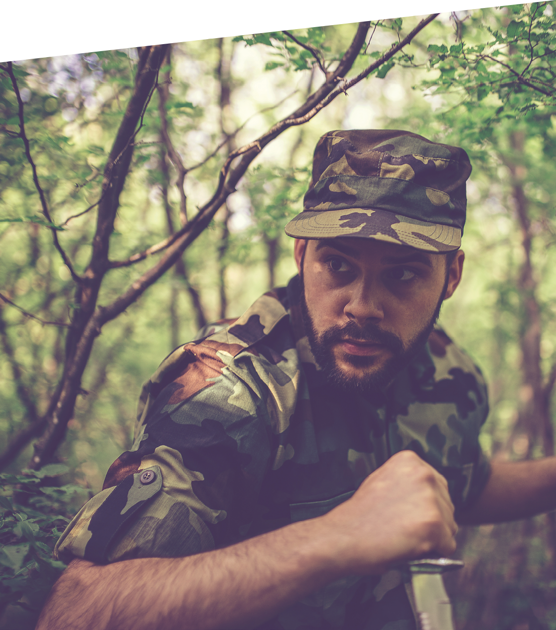 Soldier skulking in the forest ready to attack. He is holding a knife in his hand, and is prepared to attack.